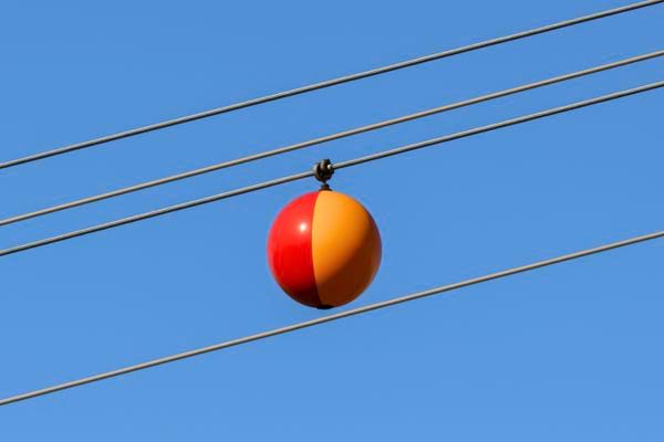 Une boule orange et rouge est accrochée à des lignes électriques dans un ciel dégagé.
