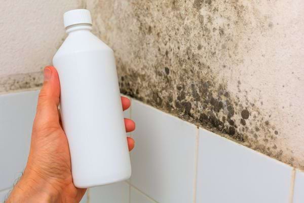 Bouteille blanche tenue devant un mur couvert de moisissures.