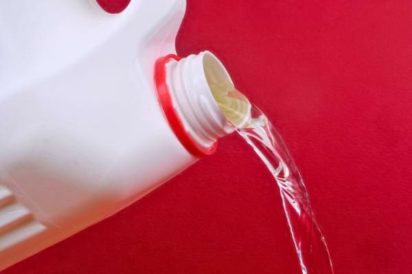 Un liquide transparent est versé depuis un bidon blanc sur fond rouge.