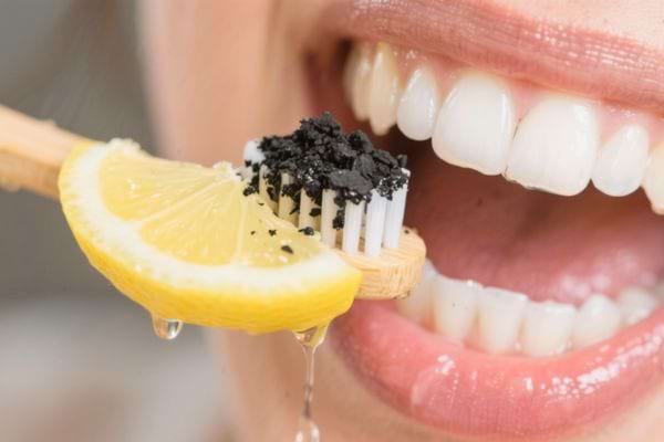 Un citron avec du charbon sur une brosse à dents près d’une bouche.