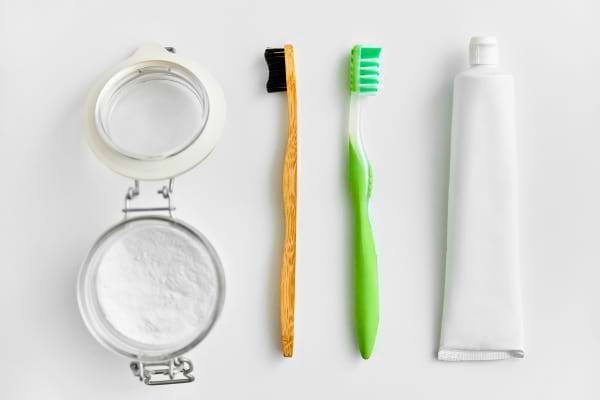 Un pot de bicarbonate, deux brosses à dents et un tube de dentifrice alignés.