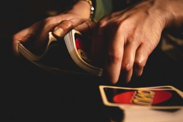 Des mains melangent un paquet de cartes Uno sur une table sombre.