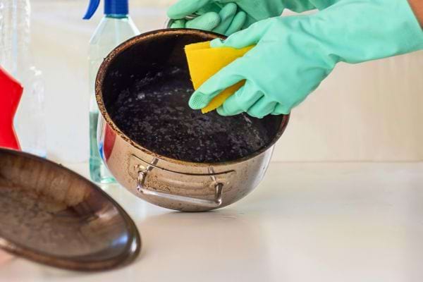 Nettoyage d’une casserole brûlée avec une éponge.