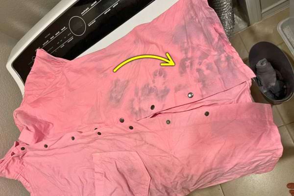 Une chemise rose tachée de traces sombres avec une flèche jaune indiquant les marques.