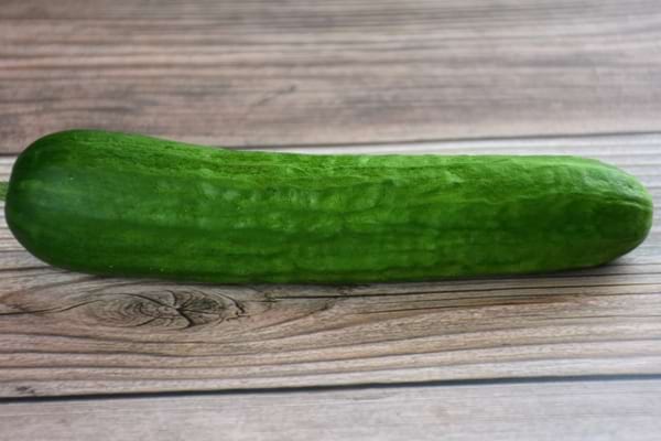 Un concombre entier allongé repose sur une table en bois.