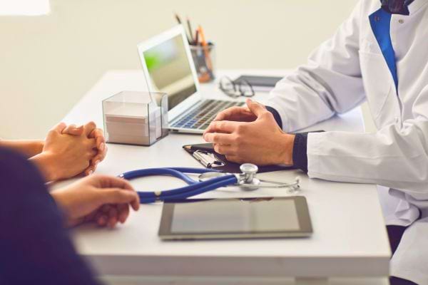 Un médecin discute avec un couple, stéthoscope et tablette posés sur la table.