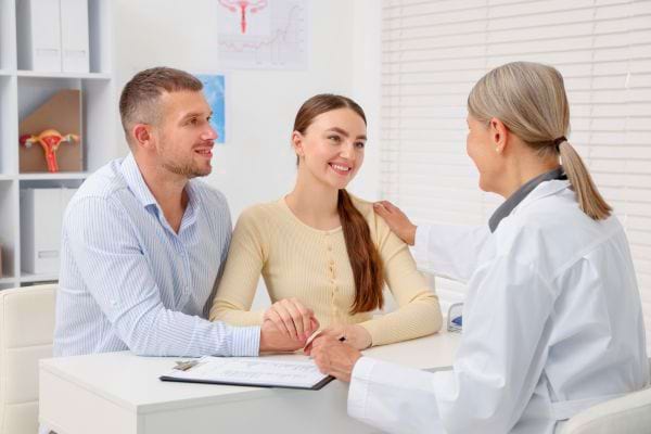 Un couple souriant tient ses mains pendant qu’un médecin leur parle avec bienveillance.