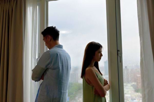 Un couple se tient dos à dos devant une grande fenêtre.