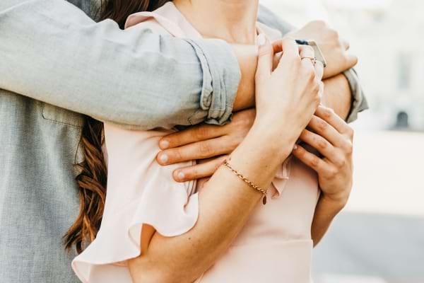 Un couple s’enlace tendrement, les bras de l’homme entourant la poitrine de la femme.