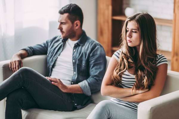 Un couple assis sur un canapé se regarde avec froideur.