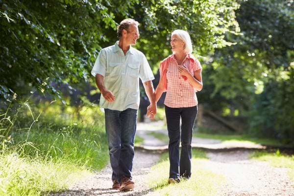 Un couple senior marche main dans la main en pleine nature.