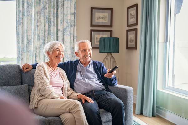 Un couple âgé sourit en regardant la télévision sur un canapé.