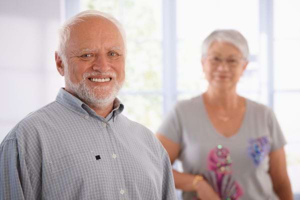 Homme âgé souriant avec une femme en arrière-plan.
