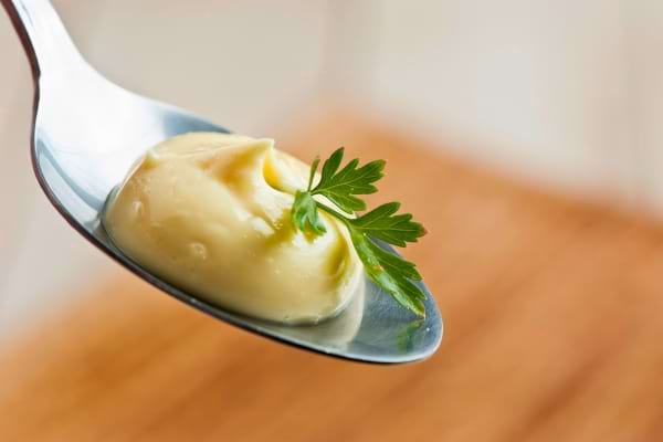 Une cuillère présente une portion de mayonnaise décorée d’une feuille de persil.