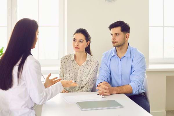Un médecin explique quelque chose à un couple attentif assis en face d’elle.