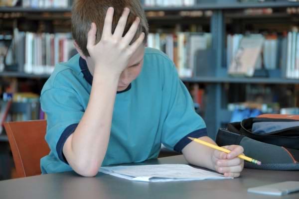 Enfant concentré, la main sur la tête, travaillant sur ses devoirs.