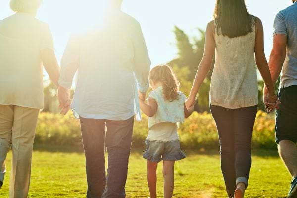 Famille multigénération marche dans un champ en se tenant la main.