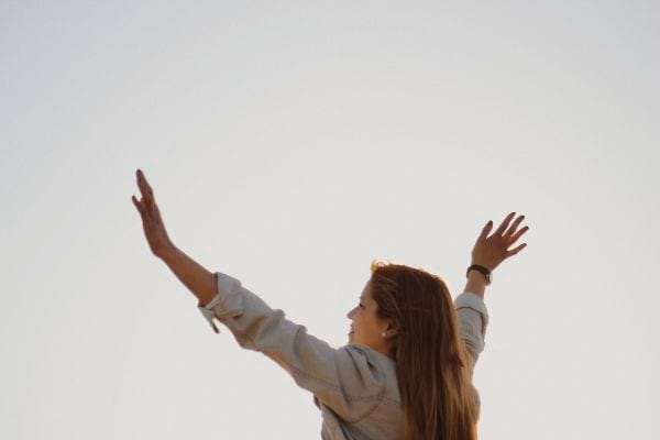 Une femme lève les bras vers le ciel, de dos.