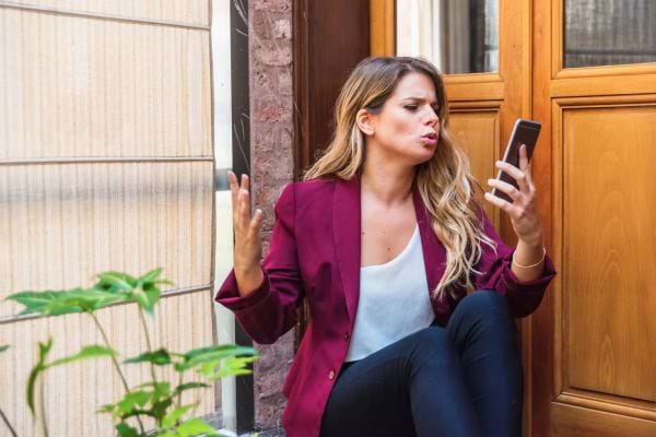 Une femme assise devant une porte exprime sa colère en regardant son téléphone.