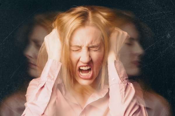 Une femme blonde crie de colère en tenant sa tête avec les deux mains.