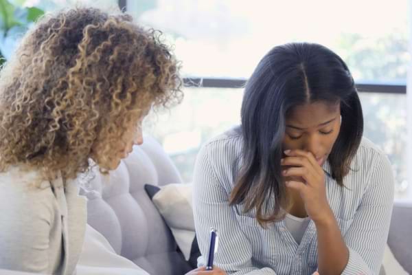 Deux femmes discutent, l’une semble réconforter l’autre préoccupée.