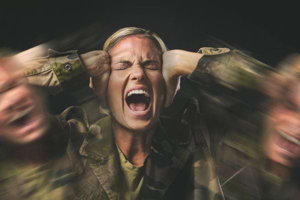 Une femme en uniforme militaire criant en se tenant la tête.