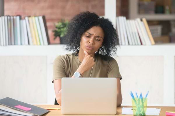 Une femme pensive regarde son ordinateur en réfléchissant.