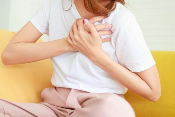 Une femme en t-shirt blanc tient sa poitrine avec les deux mains, semblant souffrir.