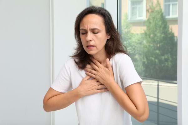 Une femme tient sa poitrine avec les deux mains, visiblement gênée par une douleur thoracique.