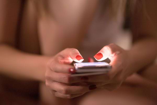 Une femme écrit sur son téléphone la nuit, éclairée par l’écran.