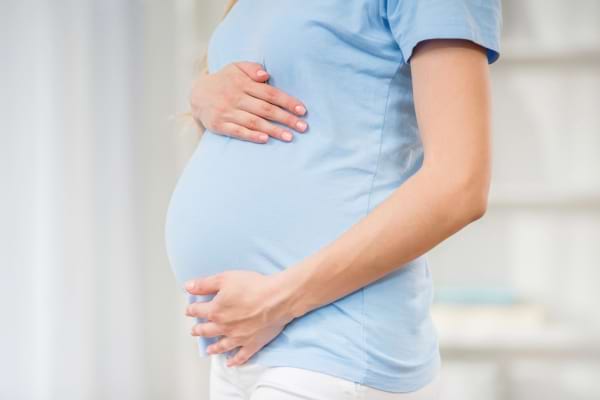 Une femme enceinte tient son ventre arrondi avec ses mains.