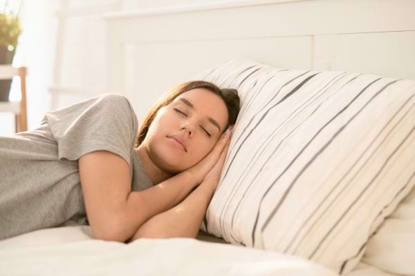 Une jeune femme dort paisiblement dans un lit, la tête posée sur un oreiller à rayures.