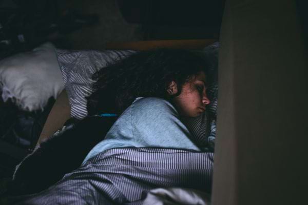 Une femme dort paisiblement dans un lit sombre, couverte d’une couette.