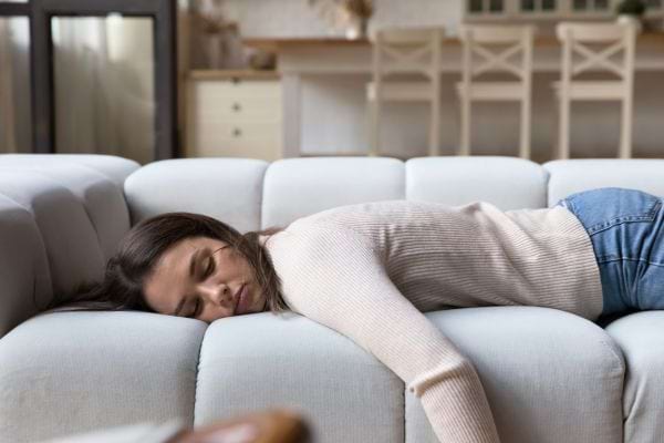 Une femme épuisée dort sur le canapé, le visage tourné contre le coussin et le corps allongé.