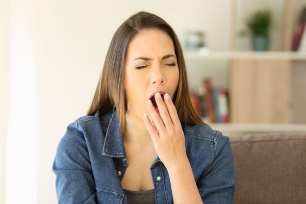 Une femme assise bâille largement, signe de fatigue ou de somnolence.