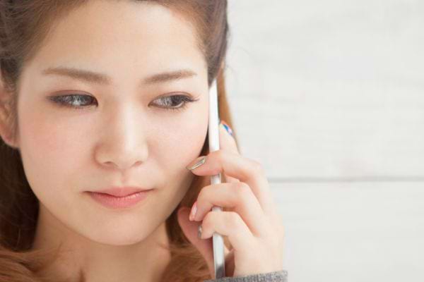 Une jeune femme tient son téléphone à l’oreille en écoutant attentivement.