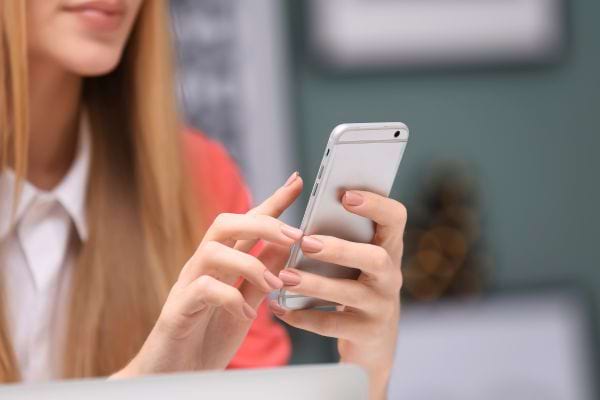 Une femme utilise son smartphone avec ses deux mains en intérieur.