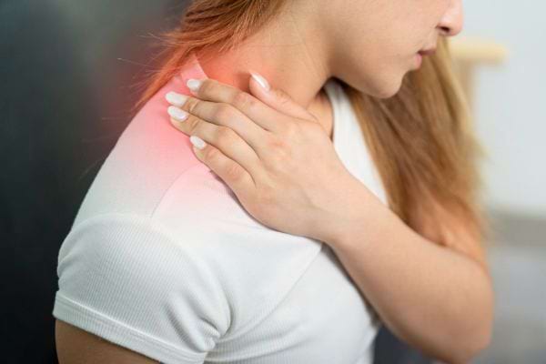 Une femme touche son épaule rouge et douloureuse avec sa main gauche.
