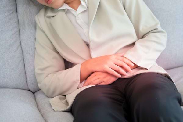 Une femme assise sur un canapé tient son ventre à cause de douleurs abdominales.
