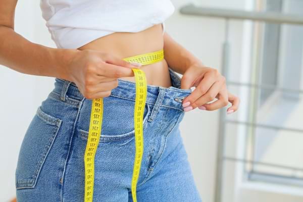 Une femme mesure son tour de taille avec un mètre ruban jaune, signe de suivi minceur.