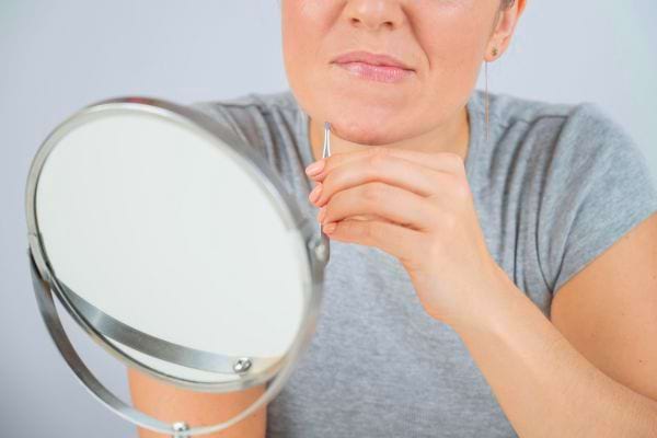 Femme fronçant les sourcils en s’épilant le menton avec une pince.