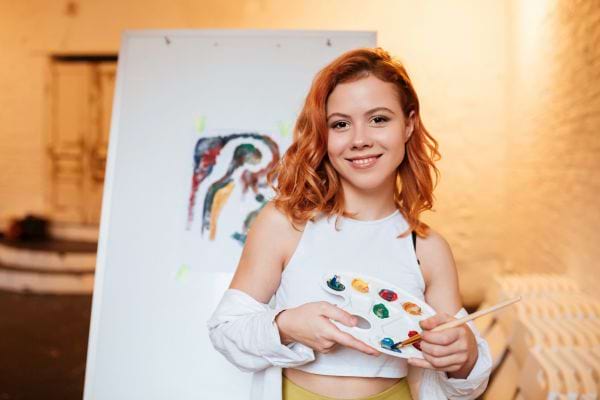Une jeune femme souriante tient une palette de peinture.