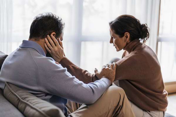 Une femme console un homme abattu en le prenant par le visage.