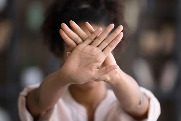 Une femme fait un signe de refus avec ses mains croisées devant elle.