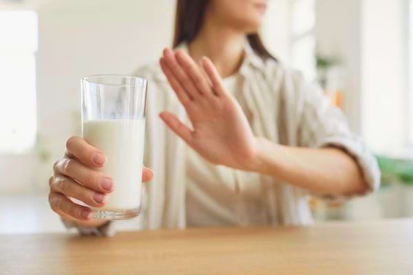 Une femme repousse un verre de lait avec la main, signe de refus clair.