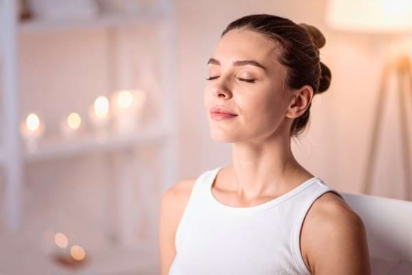 Une femme assise les yeux fermés respire profondément, profitant d’un moment de détente.