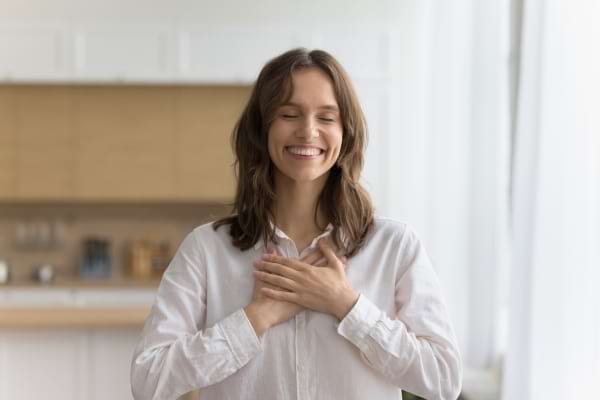 Une femme sourit les yeux fermés, les mains posées sur sa poitrine en signe de gratitude.