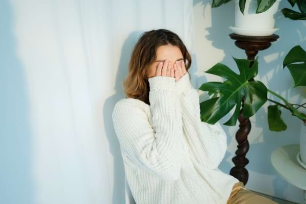 Une femme timide cache son visage avec ses mains dans un geste pudique.