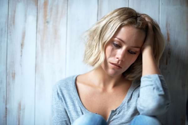 Une femme assise seule paraît triste, la main posée contre sa tempe.