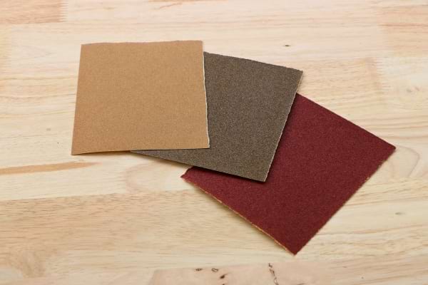 Trois feuilles de papier abrasif posées sur une surface en bois clair.